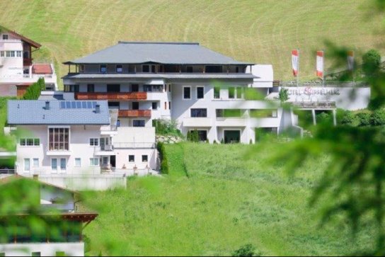 Das Hotel Gipfelherz von außen, im Vordergrund grüne Wiesen, dahinter die Berge