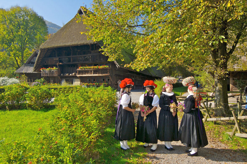 Trachtenträgerinnen vor dem Vogtsbauernhof in Schwarzwälder Tracht mit Bollenhut