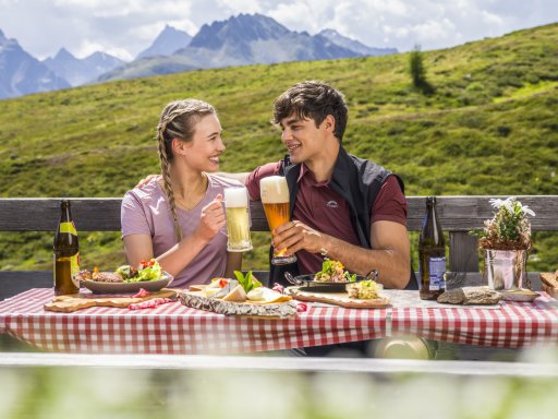 Vier Menschen bei der Jause mit Milch, Wurst und Käse auf der Alm