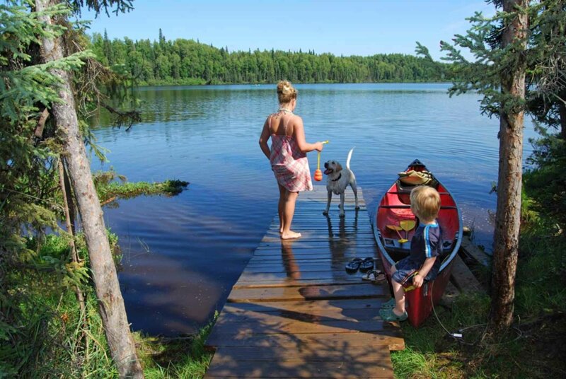 Frau und Kind spielen mit einem Hund an einem See
