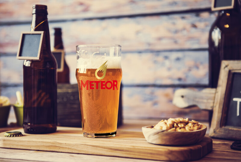 Brettchen mit Bierflasche, Glas mit Meteor-Aufschrift und Nüssen